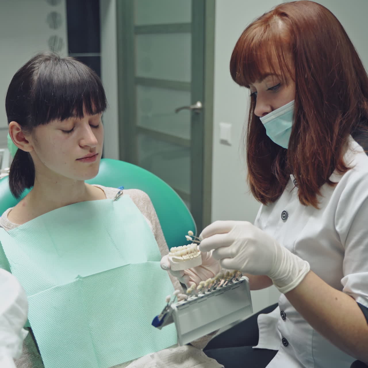Friendly dentist showing jaw layout to a patient girl sitting in the stomatology clinic. Professional dentist explaining to female patient correct tooth brushing on the dental model