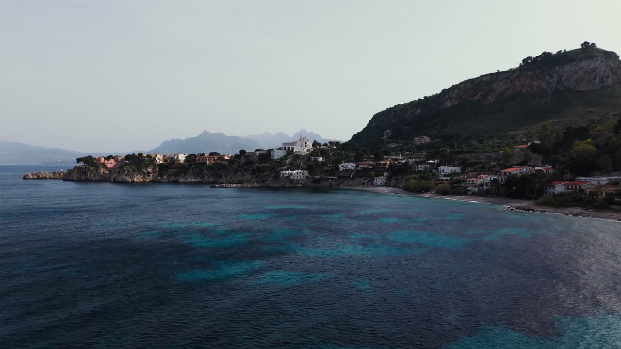 Drone aerial view of the Sicilian coastline near Porticello and Capo Zafferano with clear turquoise waters, coastal buildings, and surrounding green hills