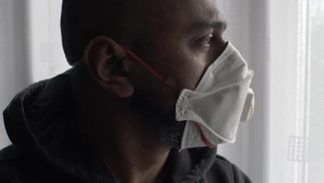 adult asian male wearing ffp three mask indoors looking through curtains