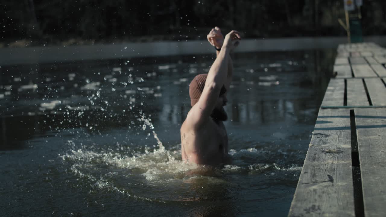 Kaukasisk voksen mand springer i en frossen sø fra badebroen om vinteren.