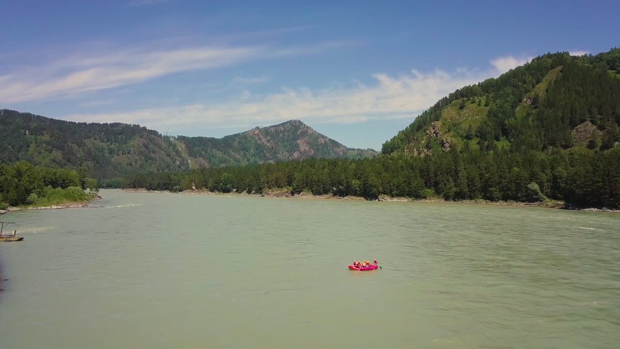 Volo aereo su fiume di montagna. Visibili anche foresta di conifere, rapide del fiume, la riva del fiume e una barca rossa.