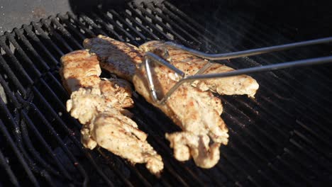 organic chicken breasts grilling on the bbq - turning them with tongs as they cook in slow motion