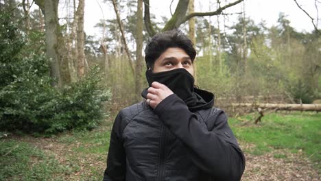 hispanic young man with a black jacket on taking off cap inside the forest