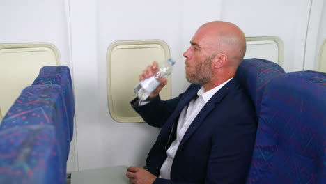 bored man on airliner plane drinking water from a bottle sitting in the cabin