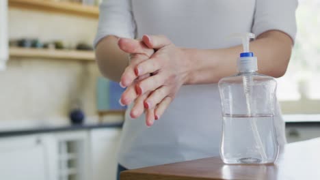 Mid-section-of-woman-sanitizing-her-hands-at-home