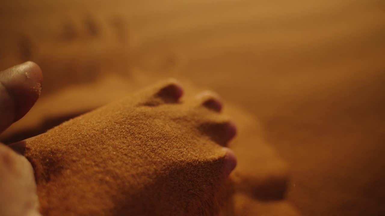 Close-up of a hand covered in fine golden Sahara desert sand, highlighting texture and warm tones under the fading evening light in Morocco