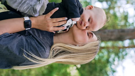 Blonde woman with her baby in hands. Loving mother kissing her child to a cheek. Vertical screen.