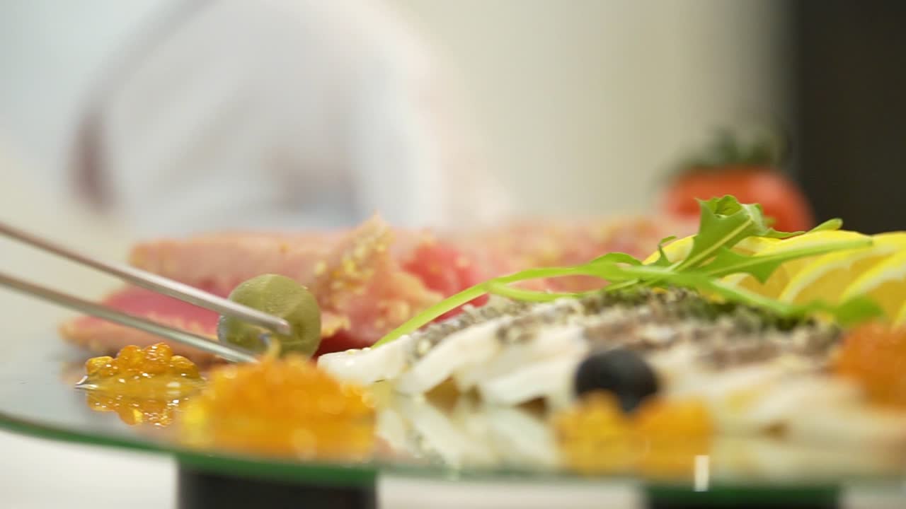 Sliced of meat and hard cheese with sesame are decorated with gooseberries, red caviar, lemon slices and cilantro leaves on the festive table before the guests arrive. Close-up.