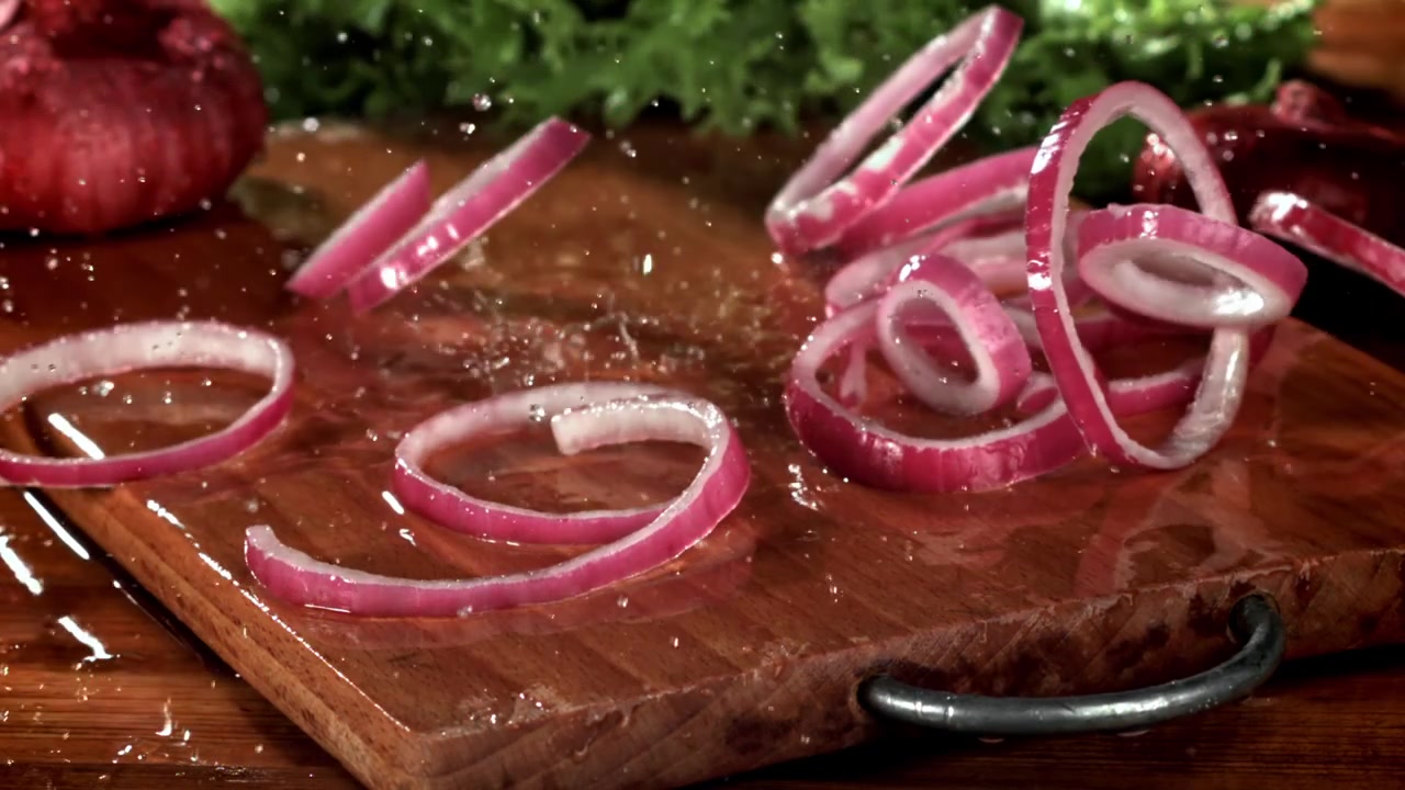 Slow Motion Red Onion Rings Falling onto Wet Wooden Cutting Board
