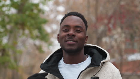 confident young man posing while chewing gum, removing hoodie in outdoor setting with bare trees in background, capturing casual confidence and street-style fashion in winter