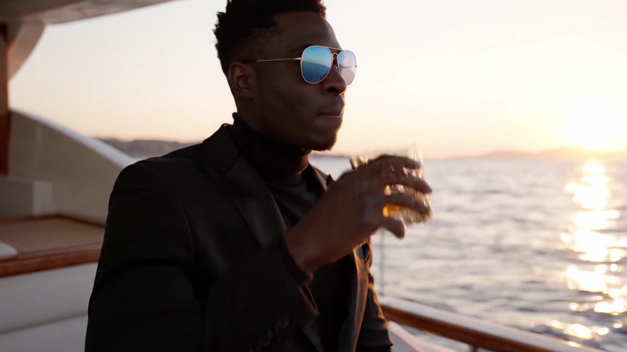 Un gentiluomo sofisticato si gode un tramonto su uno yacht di lusso mentre assapora un drink, catturando l'essenza dell'eleganza e del tempo libero in mare