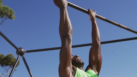 hombre afroamericano en forma haciendo ejercicio afuera, haciendo chin-ups en un marco de escalada