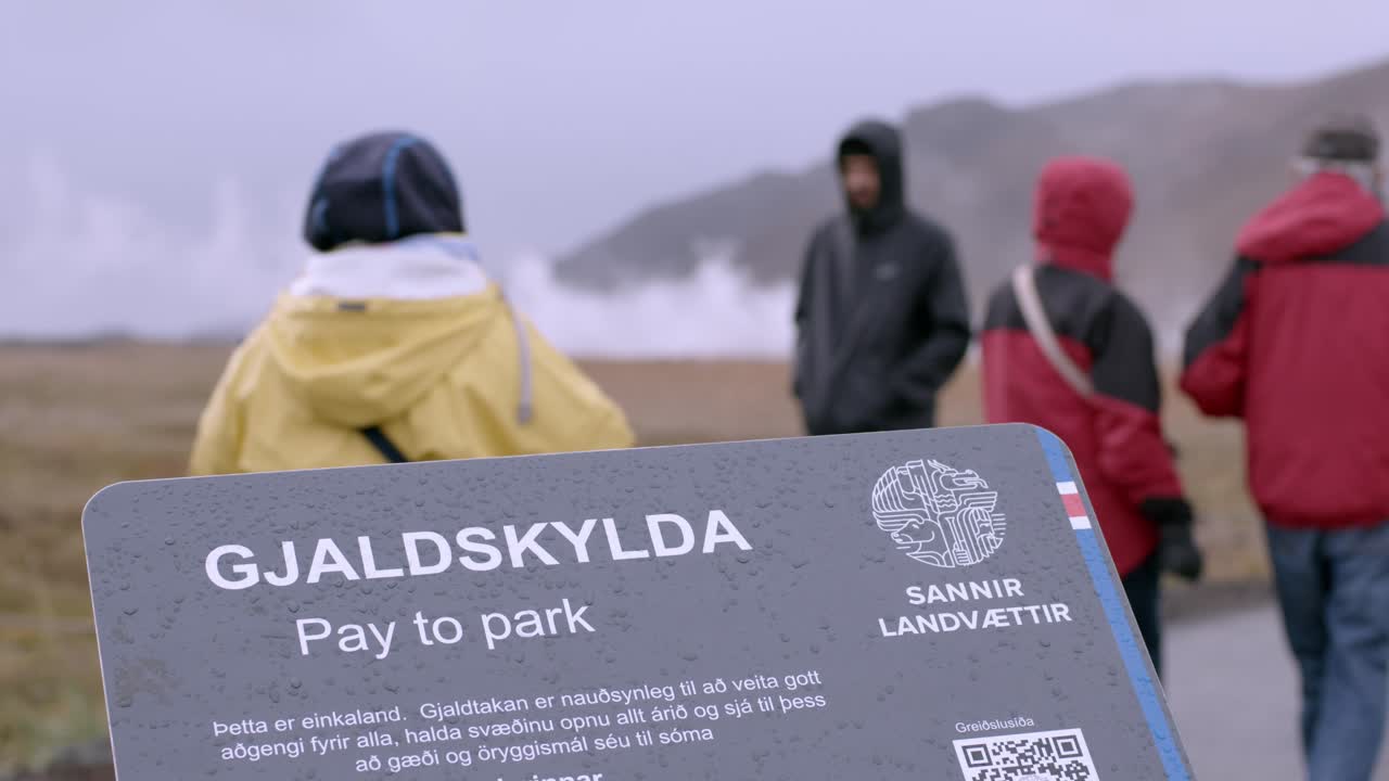 Tourists gather near a parking lot sign in Iceland’s misty and cold landscape.