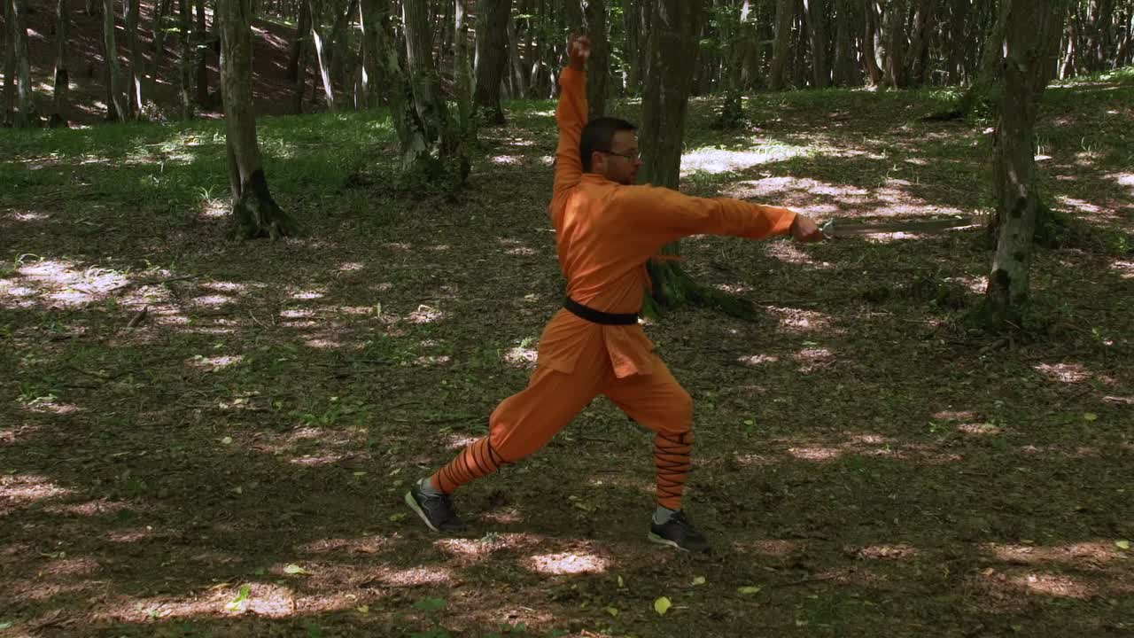Black Belter Man With Sword Doing Kung Fu Exercises In The Forest. - wide shot