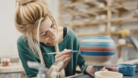 Zoom out shot of pottery artist decorating ceramic pot at pottery workshop, slow motion