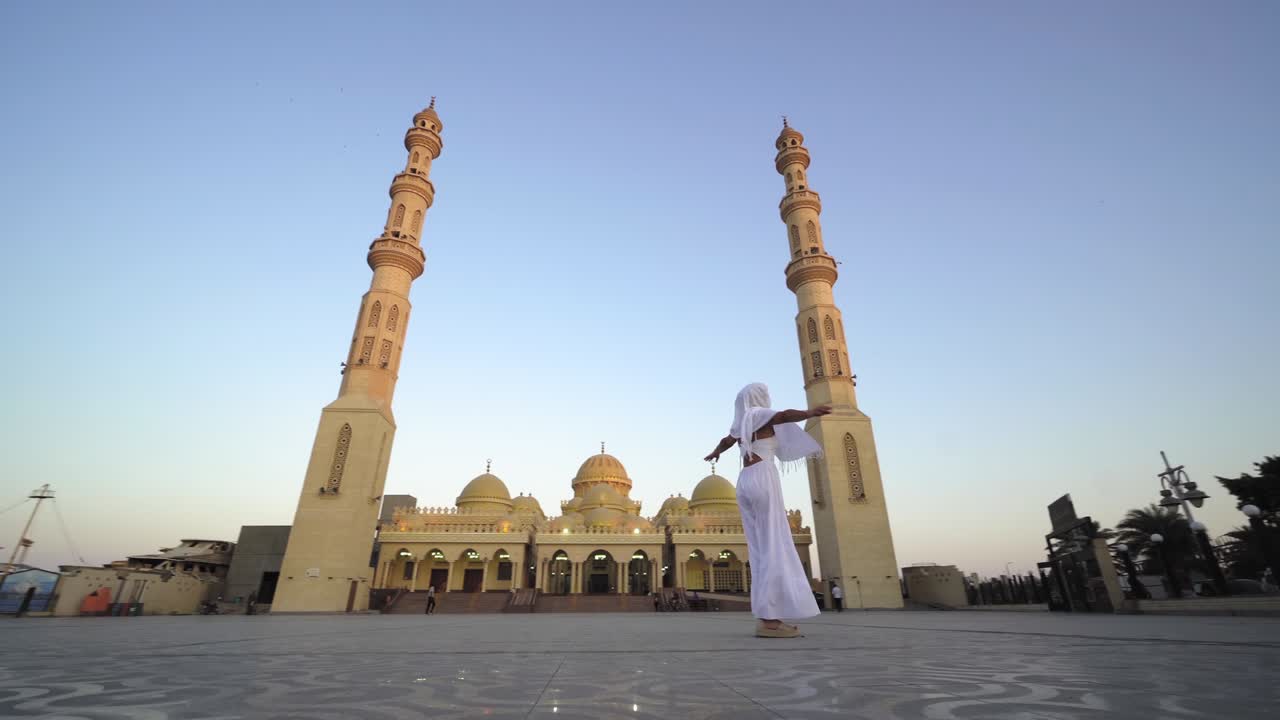 вид на закат и восход солнца мечети эль-мина с женщиной-туристкой в длинном белом платье и хиджабе, крутящейся и наслаждающейся видом на мечеть