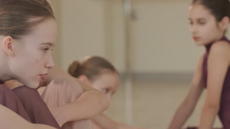 a group of young ballet students in black dancewear practicing positions in a spacious ballet studio with wooden flooring and wall-mounted barres. focused expressions and synchronized movements.