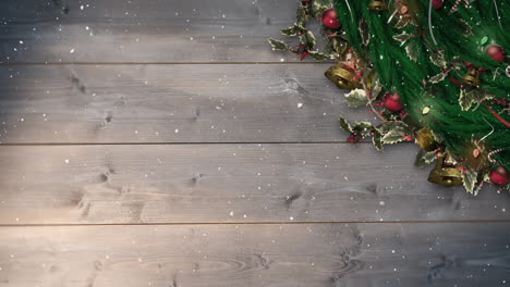 christmas decorations with bells and holly, falling snow on wooden background