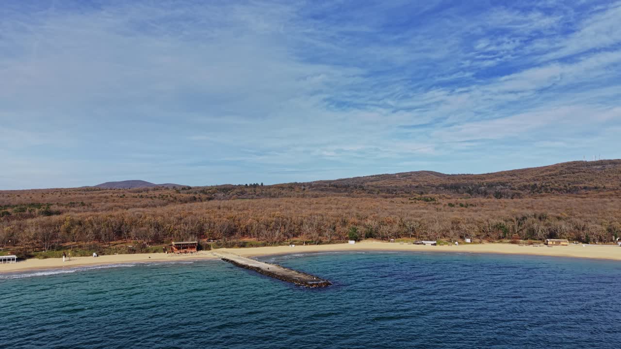 Aerial view of a serene beach and pier with wooded hills in the background