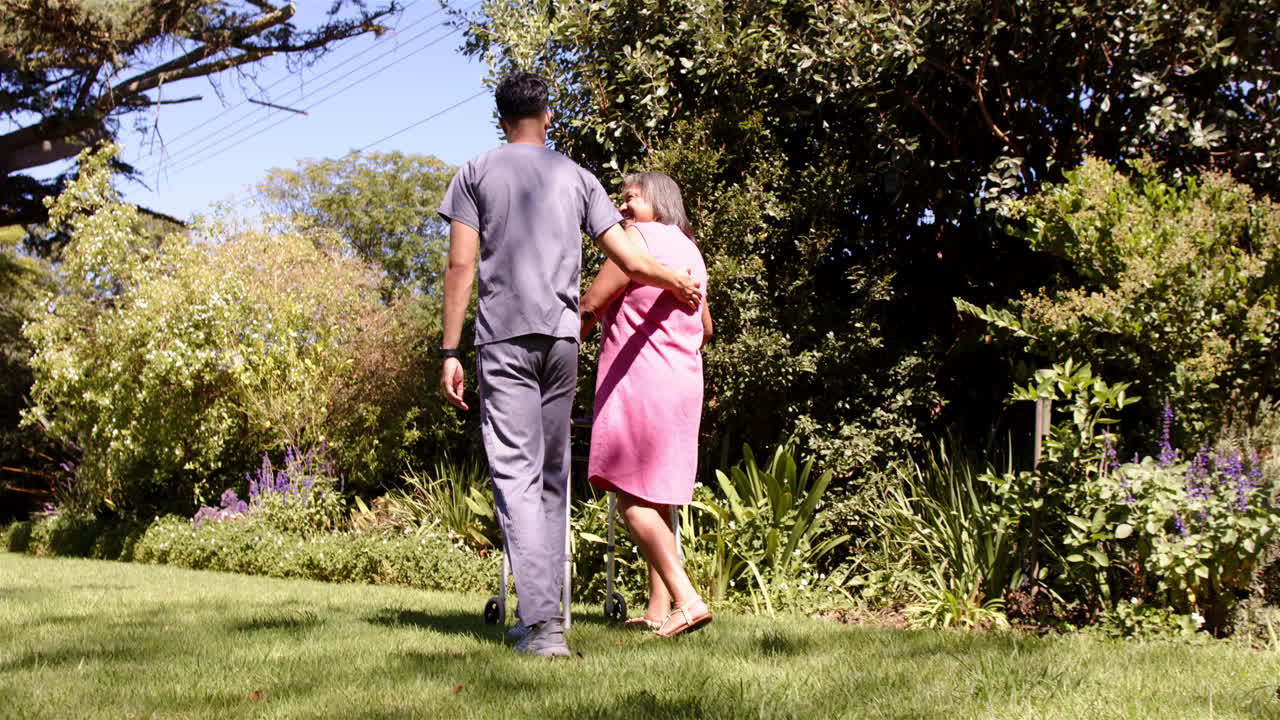 Walking in garden, male physiotherapist supporting senior woman