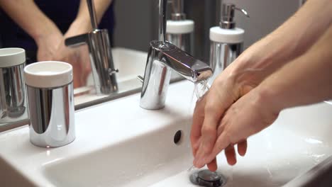 white male disinfects hands by washing them with tab water