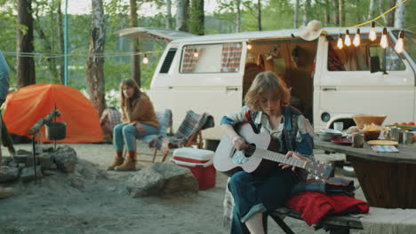 woman playing guitar at campsite with friends