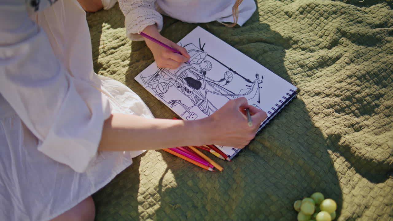 夏のピクニックでアルバムに手描きの絵を描く親子のクローズアップ。気楽な家族。
