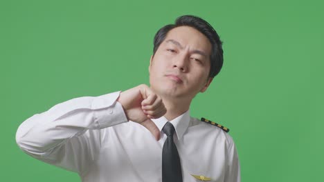 close up of asian man pilot showing thumbs down gesture to camera while standing in the green screen background studio