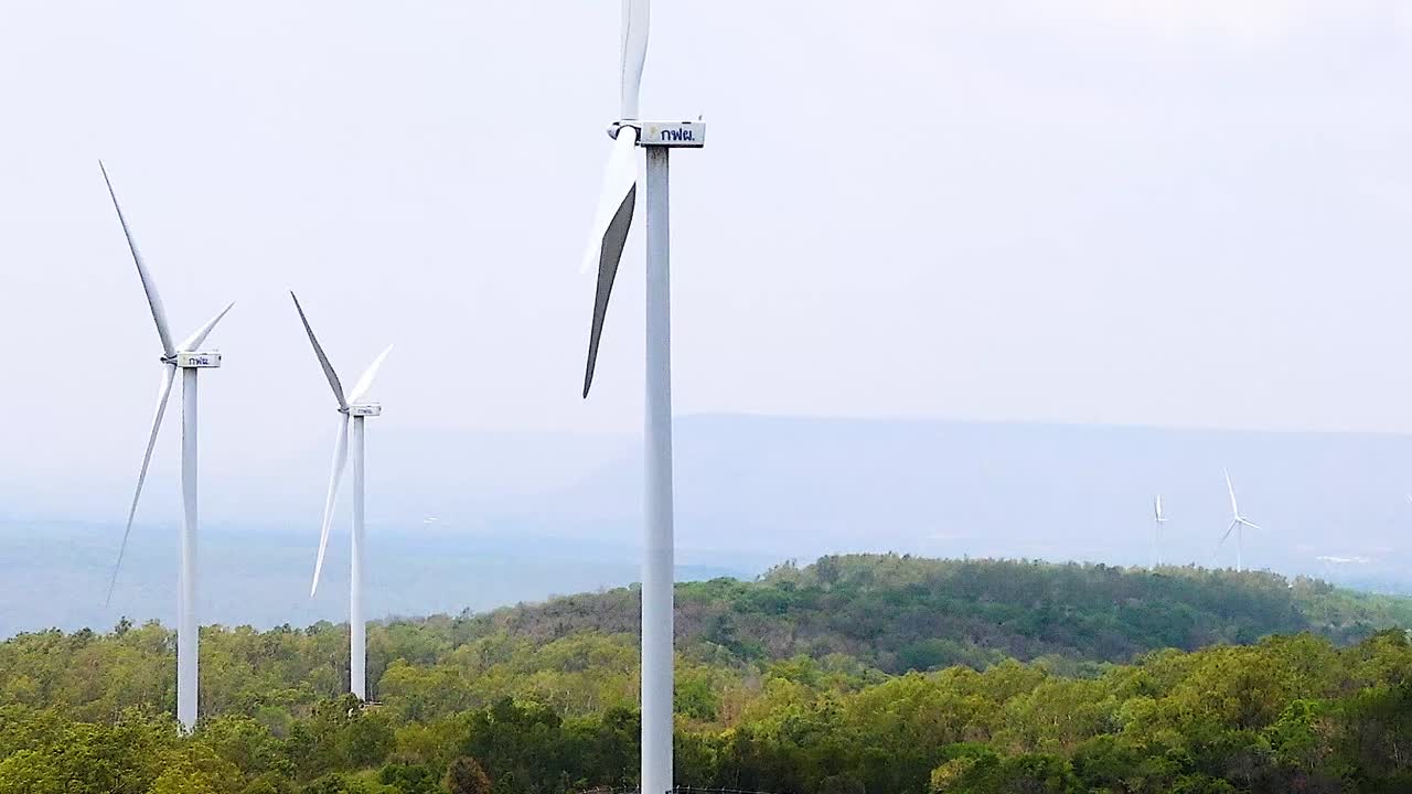 A series of wind turbines stand tall over a verdant landscape with distant hills and a clear sky.