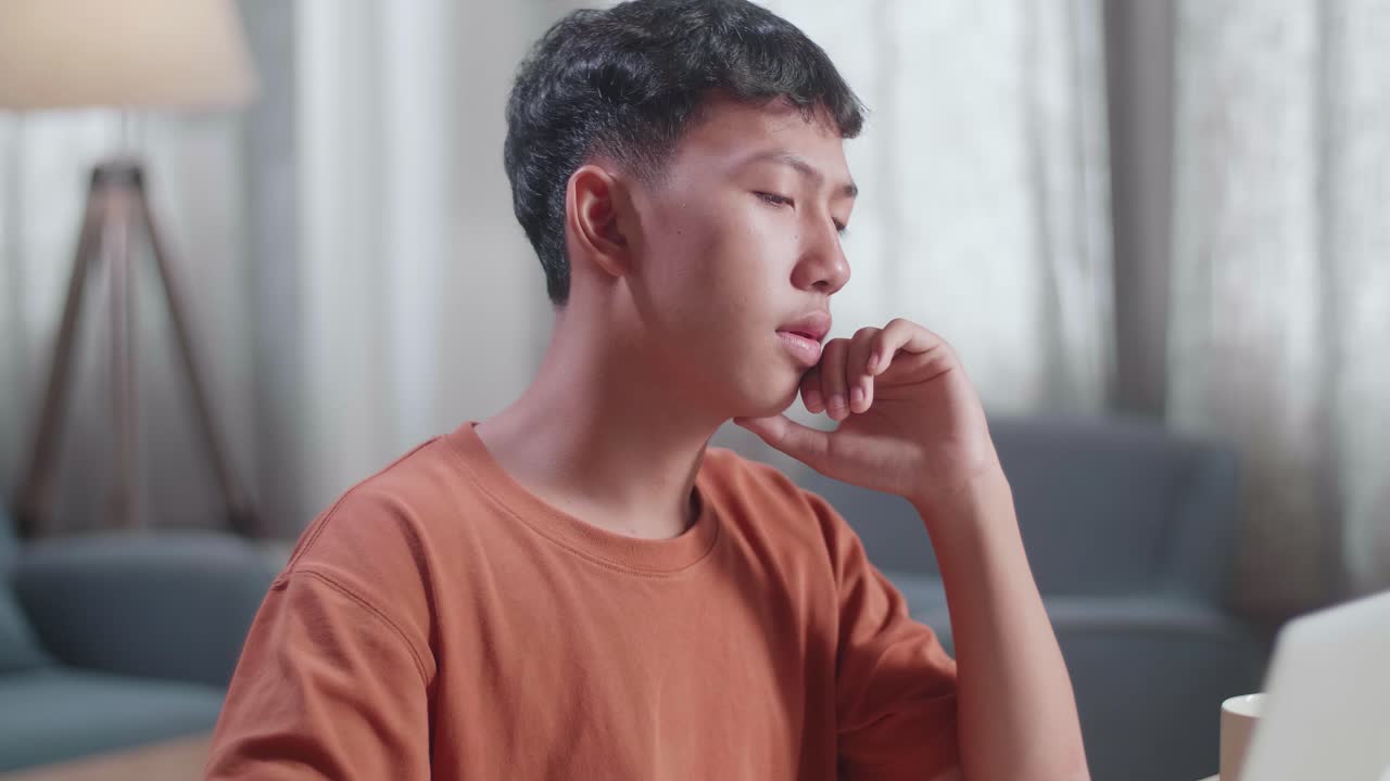 아시안 소년 신발 디자이너가 집에서 노트북으로 작업하는 동안 지표손가락을 올리는 것을 생각하고 있습니다.