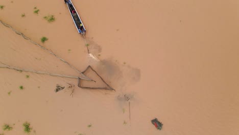 Fishermen-exit-in-boat-near-arrow-head-fishnet-traps-stirring-up-brown-muddy-flooded-waterways-of-the-Mekong-delta