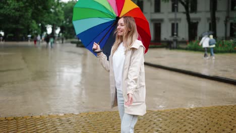 una mujer rubia feliz deja que la refrescante lluvia de primavera caiga sobre ella en la calle