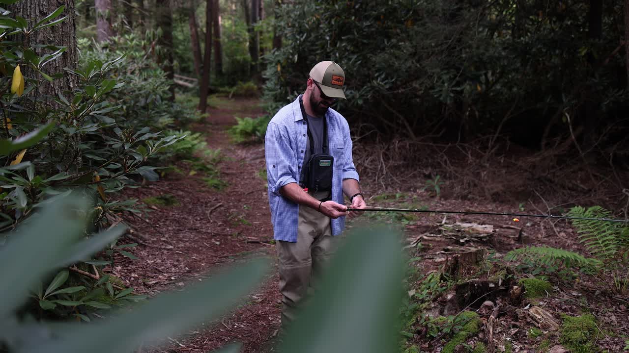 Slow Motion footage of a Fly Fisherman in the Pocono Mountains in Pennsylvania preparing his gear for an afternoon on the stream. Camera pans up from foliage in the foreground.