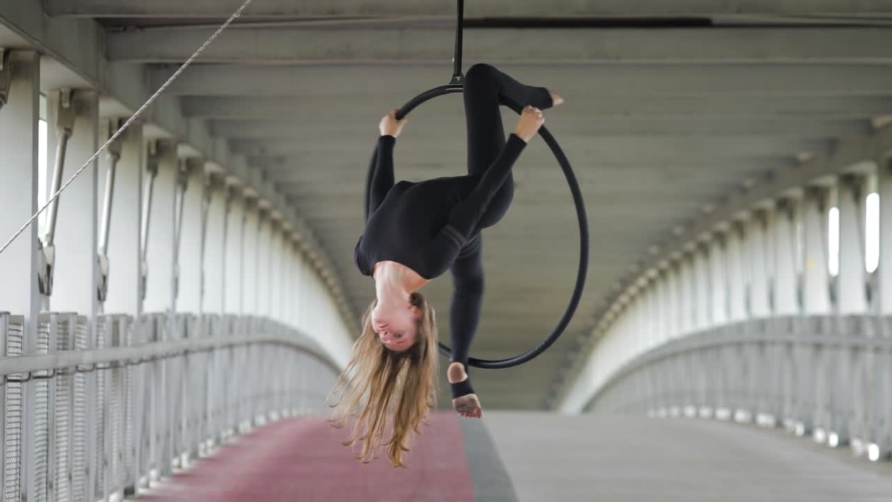 Acrobat girl hanging from a hoop on an urban bridge
