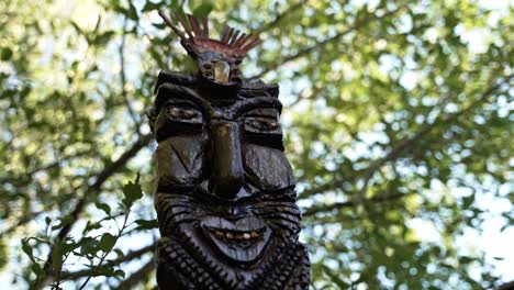 una gran estatua cultural de un dios tiki con un gran árbol verde de hojas en el fondo