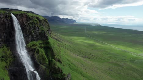 aerial view of a waterfall along the ring road in iceland. the waterfall cascades down rugged cliffs into a river below, surrounded by iceland's natural landscape.