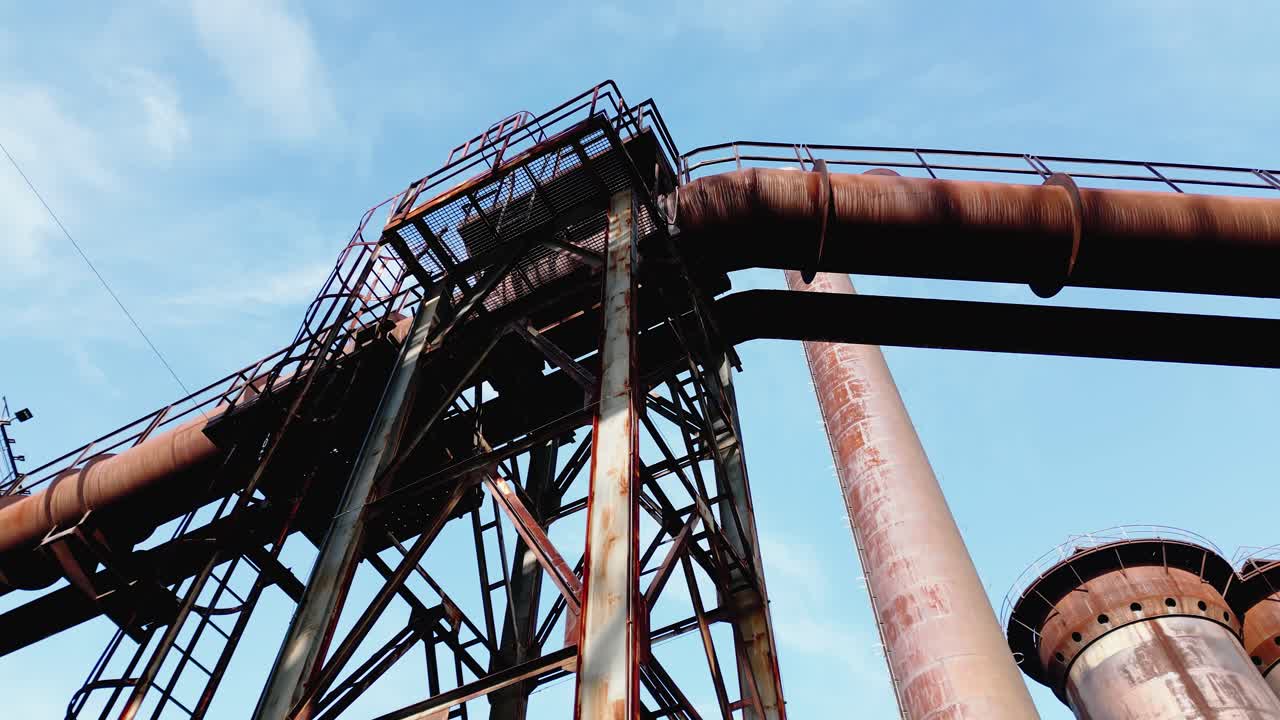 Struttura industriale arrugginita con grandi tubi e una intelaiatura metallica contro un cielo azzurro limpido