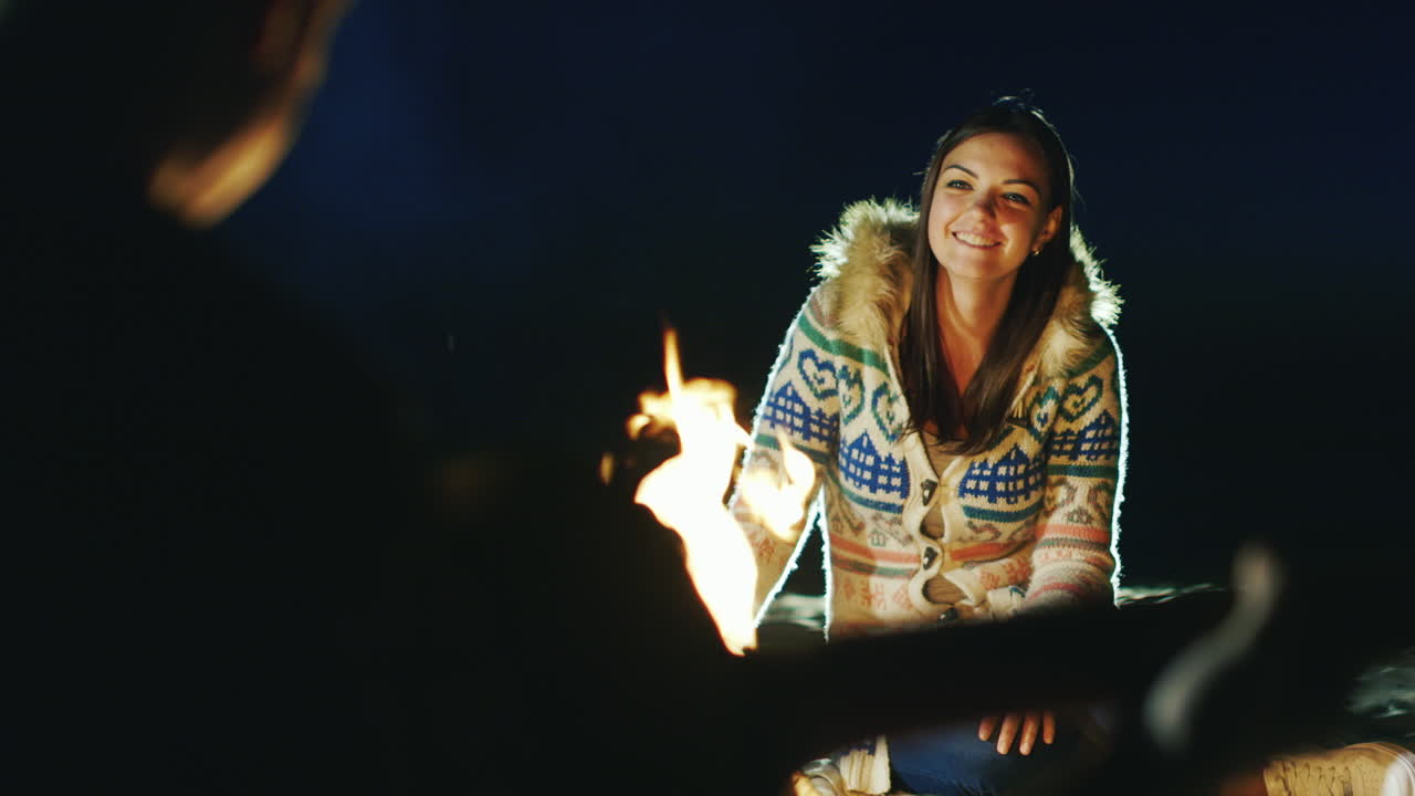 불 옆에서 휴식을 취하는 친구들 전경에서 기타를 치는 남자