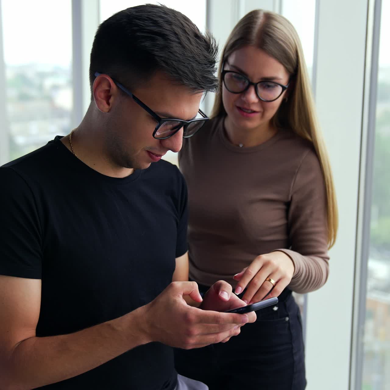 Young people in office discussing some issues during a break from work. Colleagues look at phone in man's hands talking about what they see