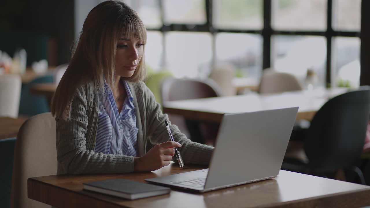 joven hermosa mujer de negocios asiática sonriente sosteniendo un café y una computadora portátil colocada en la mesa de madera en la oficina. mujer chequeando el correo o investigando mientras teletrabaja