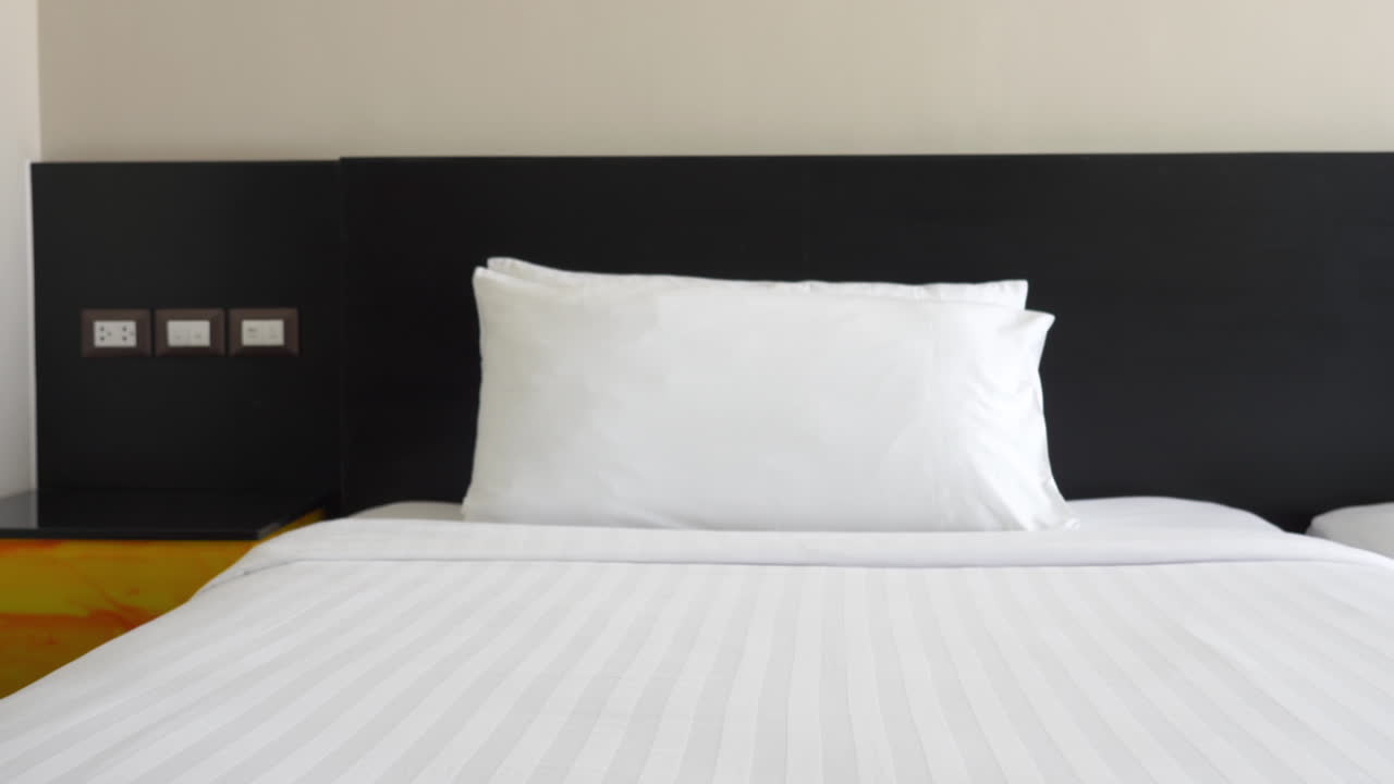 чистая белая и серая полосатая одежда, покрытая приглашающей двойной кроватью с чистыми белыми подушками и черной головной доской в спокойном отеле бизнес-класса