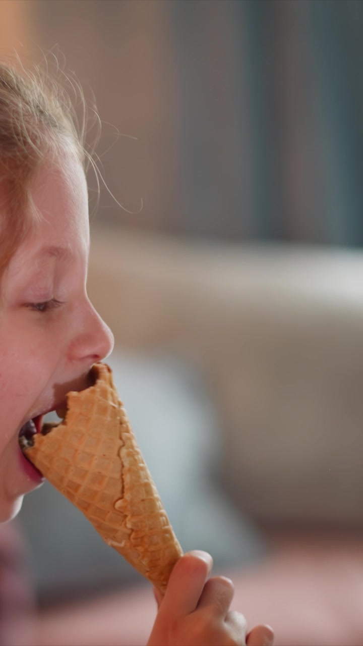 Close up of young girl enjoying ice cream cone bringing it to her mouth and taking bites. waffle texture is clearly visible as girl holds partially eaten treat. Soft indoor lighting