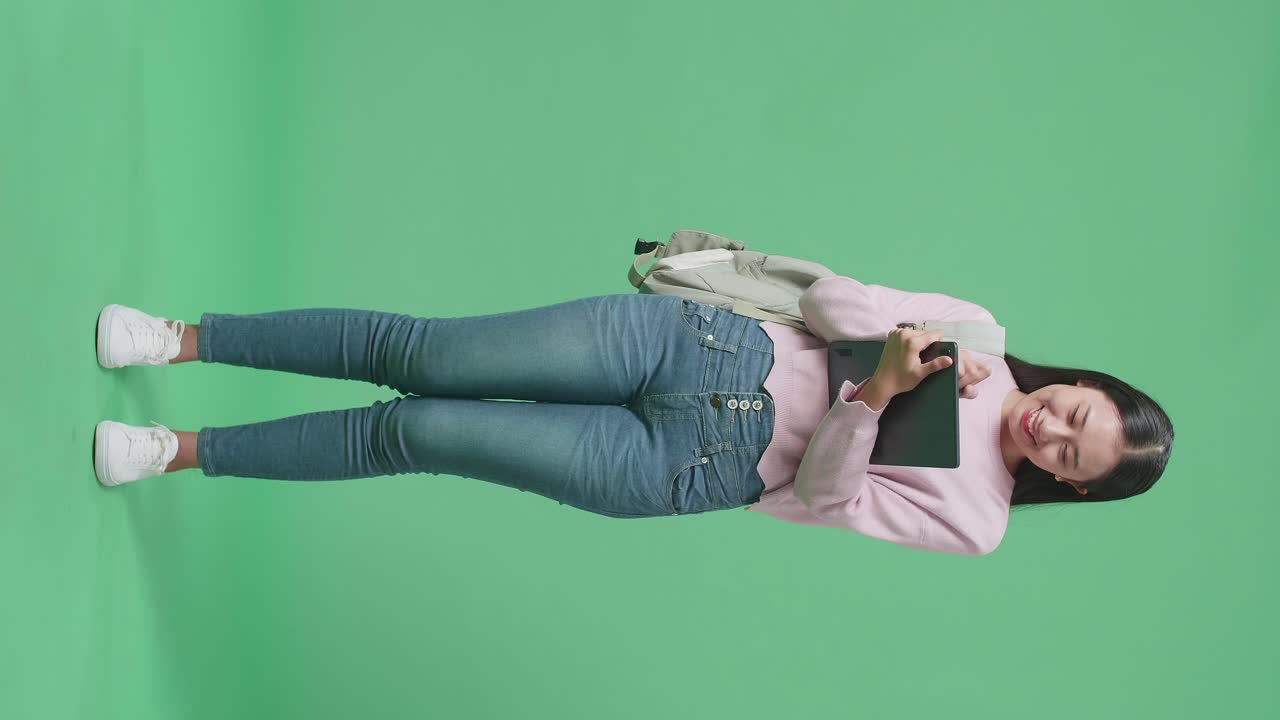 Full Body Of Asian Woman Student Writing On Tablet On Green Screen Studio