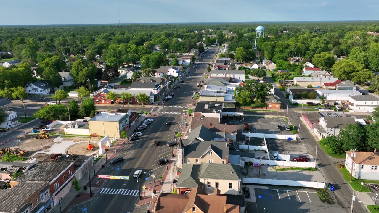 Tomada aérea de aproximação de uma cidade histórica em Egg Harbor City, Nova Jersey. Carros circulando na Main Street de uma cidade americana no verão. Árvores verdes e edifícios coloniais antigos na cidade. Plano geral