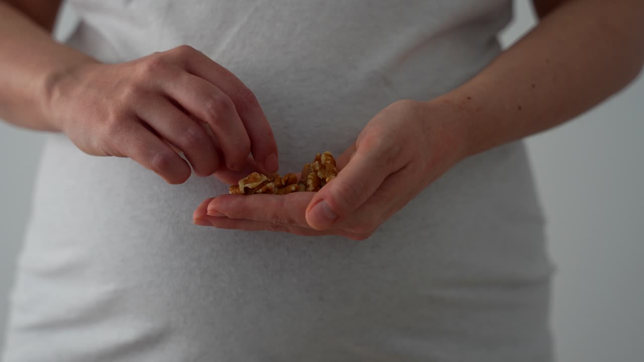 Hand of a pregnant female holding and eating a handful of walnuts