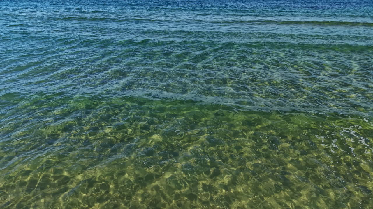 Onde calme che si infrangono dolcemente su una spiaggia serena al tramonto, con acqua cristallina che riflette tenui sfumature nella luce della sera, creando una tranquilla atmosfera costiera
