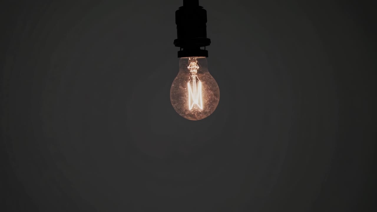Un fotogramma video scarsamente illuminato con una lampadina luminosa appesa dall'alto, ripreso da una angolazione bassa
