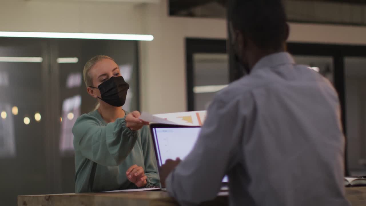 다양한 남녀 비즈니스 동료들이 얼굴 마스크를 쓰고 책상에 앉아 문서를 전달하고 있습니다.