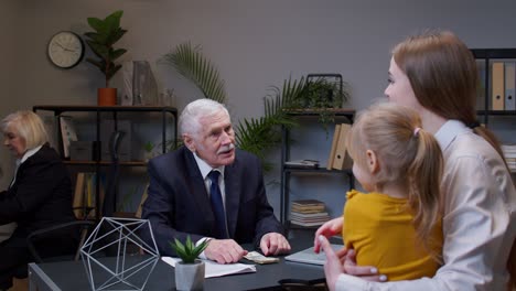 a man in a suit gives money to a woman and a girl in an office setting.