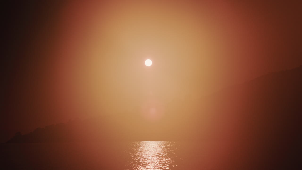 Wide shot of the sunset illuminating the sea surface, creating a bright reflection on the water